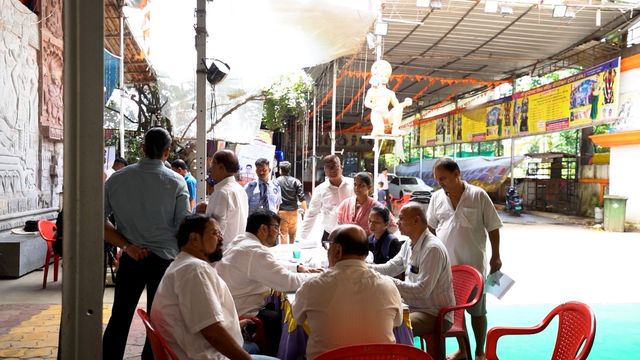 Attendees seated at the registration and consultation table under the temple's decorated entrance, with volunteers assisting
