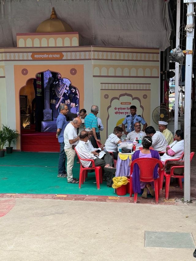 Wide view of the camp setup at the temple, with a registration table, seating and the decorated stage backdrop of Shri Budheshwar Shiv Mandir