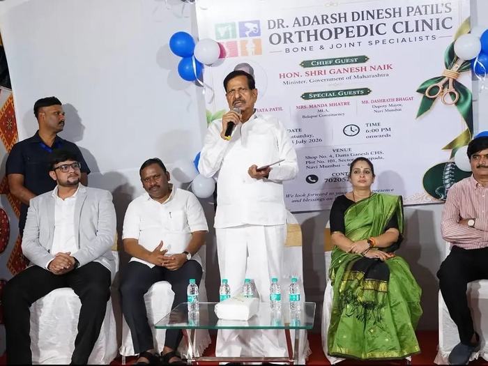 Hon. Shri Ganesh Naik, Minister, Government of Maharashtra, speaking into a microphone in front of the clinic's inauguration banner, with invited guests seated behind