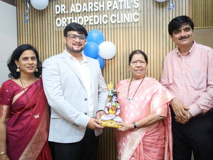 Dr. Adarsh Patil and three guests holding a small idol together beneath the clinic's wall signage on the wood-slat reception wall